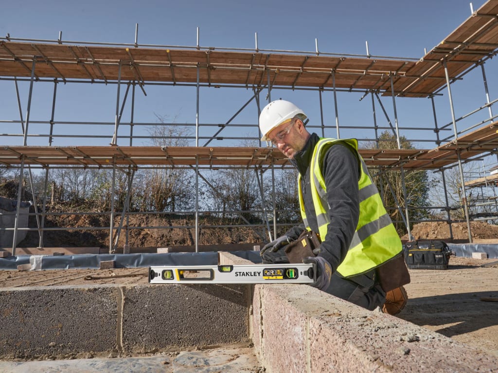 Person in construction gear using a Stanley level on a building site with scaffolding in the background. - imagen 8