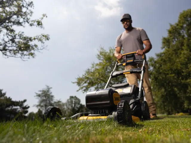 Person mowing the lawn with a DeWalt lawn mower on a sunny day, cutting grass evenly in a well-maintained garden