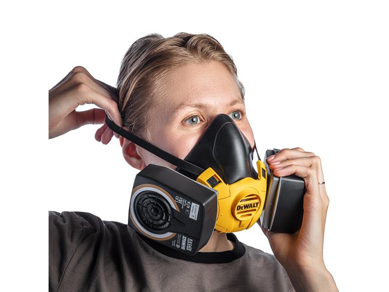 Person wearing a DEWALT half mask respirator with dual filters, adjusting the head strap for a secure fit.