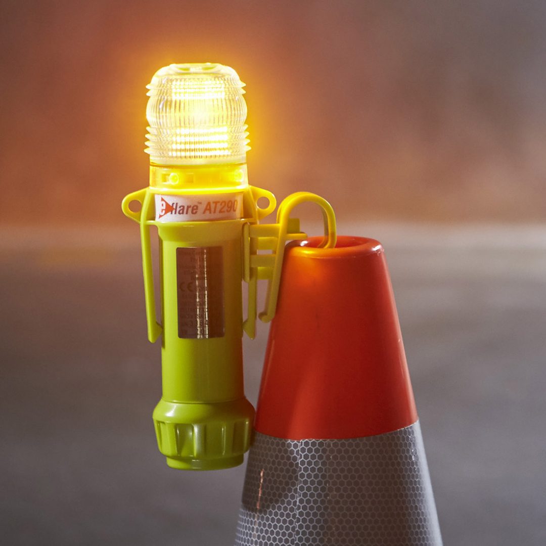 Portable yellow emergency warning beacon attached to a traffic cone and illuminated.