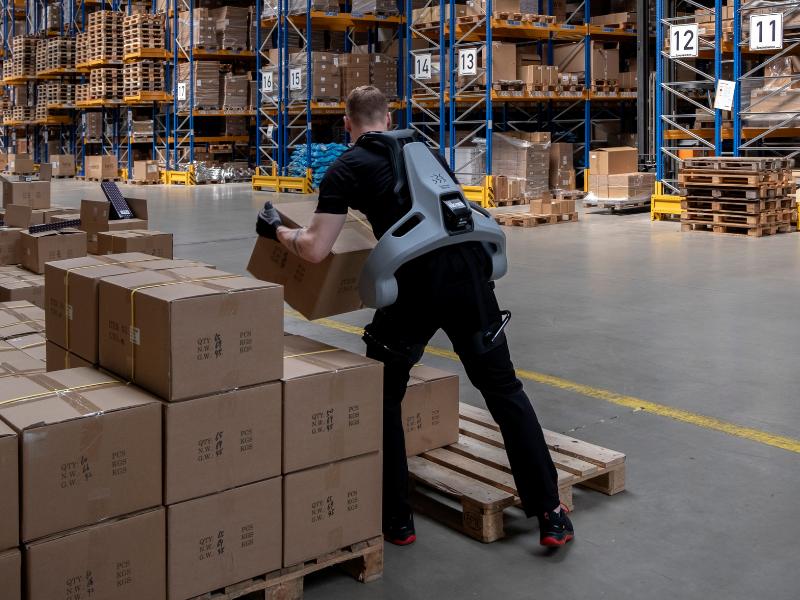 Person in a warehouse using a back support device while handling boxes.