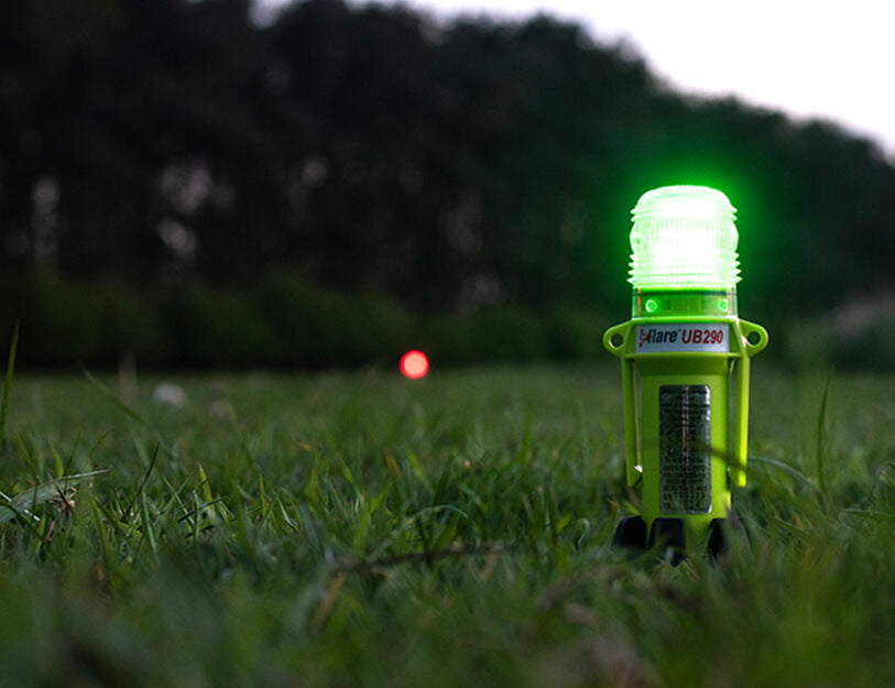Eflare UB290 Series LED Safety Beacon glowing green in a grass field at dusk, with a second red beacon visible in the background - imagen 7