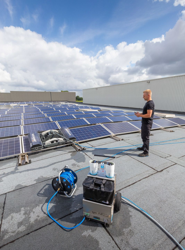 Person cleaning solar panels on a rooftop with cleaning equipment.