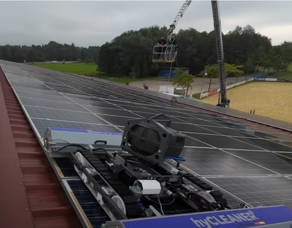 Solar panel cleaning robot on a roof with a cloudy sky and trees in the background